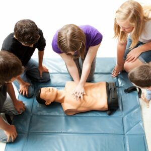 A group of people standing around an adult cpr dummy.