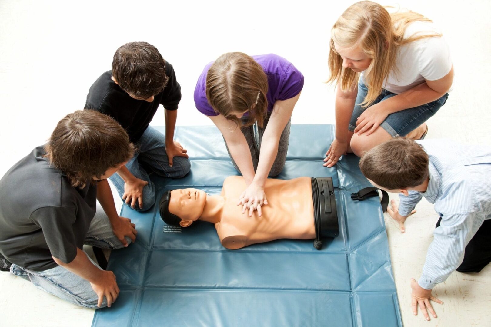 A group of people standing around an adult cpr dummy.